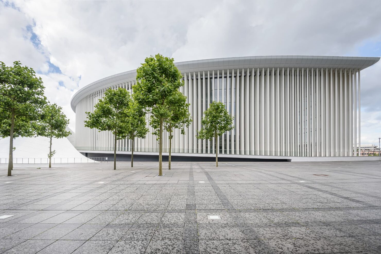 The colonnaded facade of the Philharmonie Luxembourg concert hall on the Kirchberg plateau, with trees in the plaza in front.