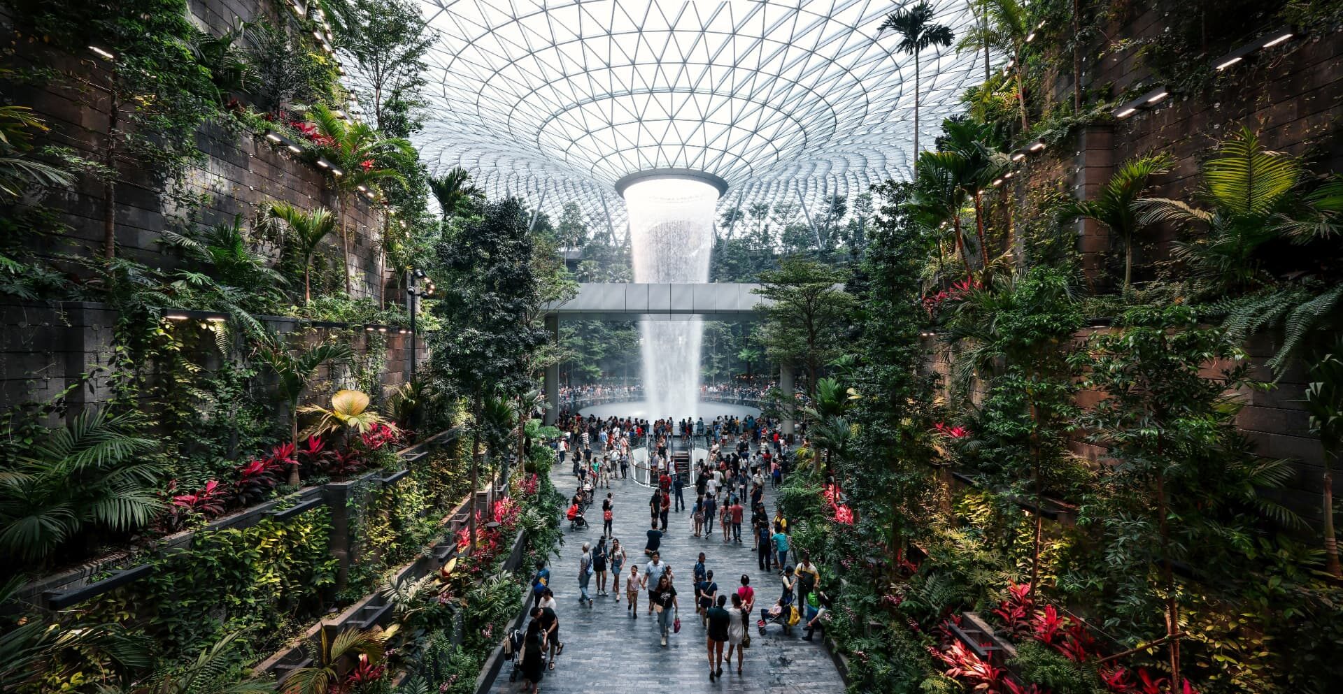 Visitors walking beneath the indoor waterfall and terraced planting under the glass dome of Jewel Changi Airport, Singapore.