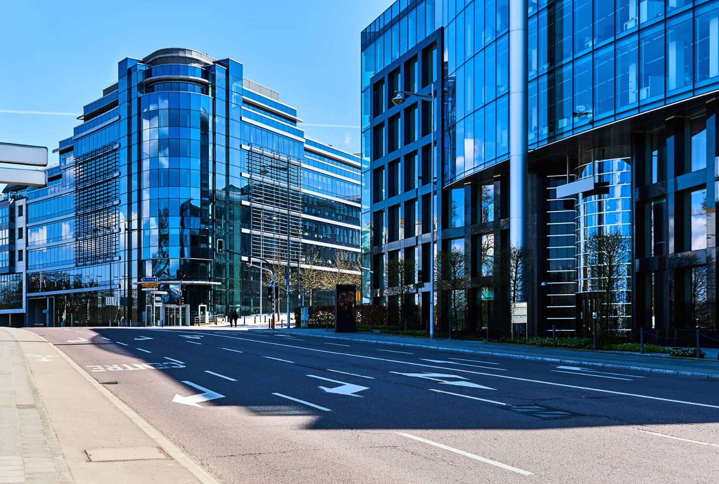 Glass office buildings on a quiet street in Luxembourg's Kirchberg financial district under a clear sky.