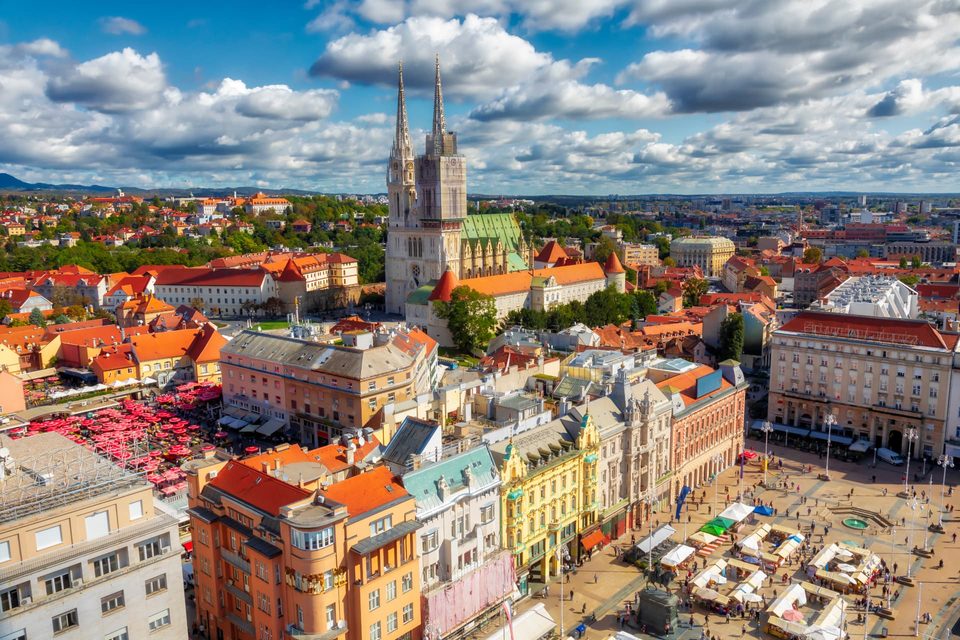 Daytime aerial panorama of Zagreb, Croatia, showing the cathedral spires and red-roofed buildings of the city.