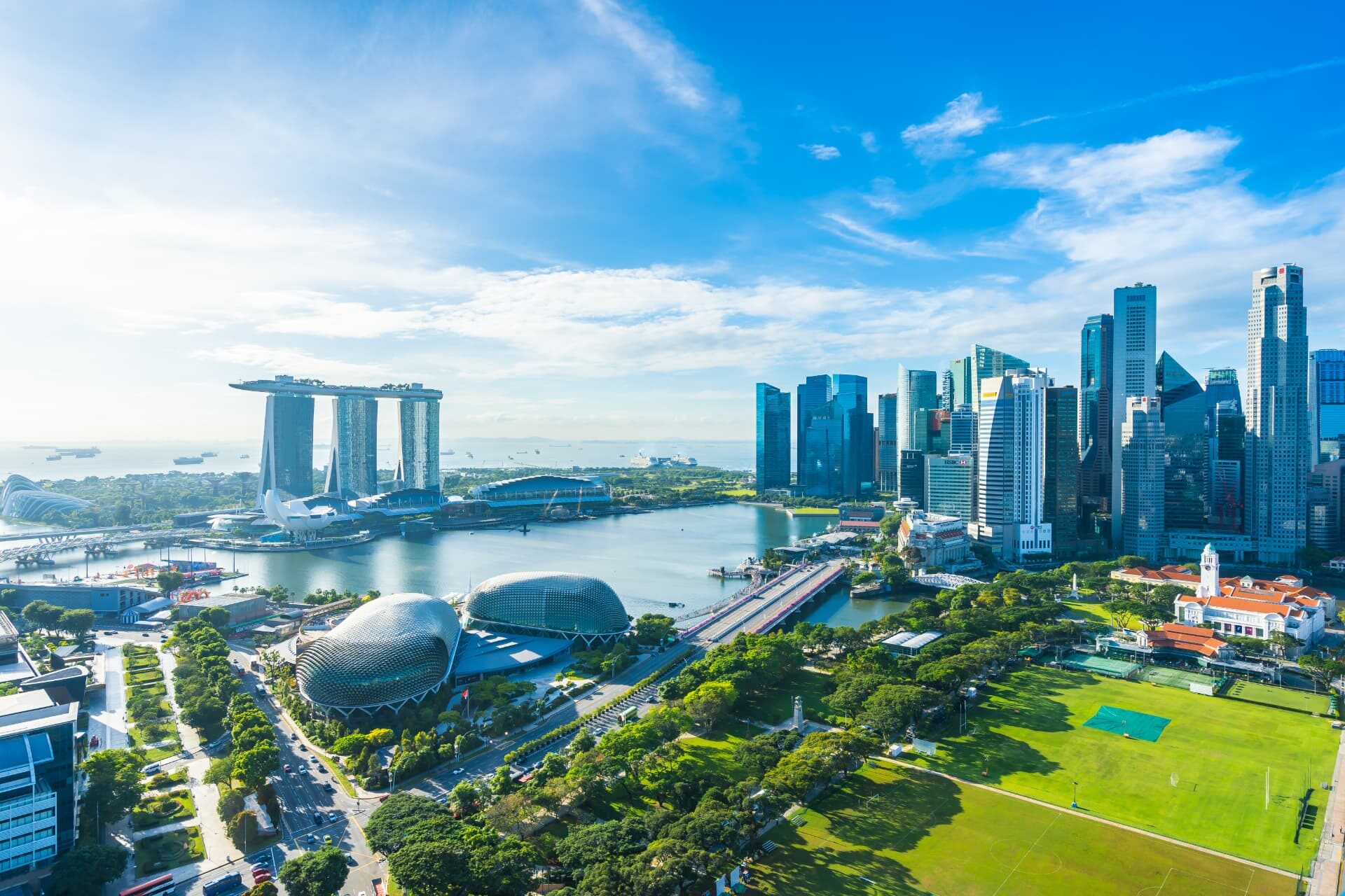 Daytime view over Marina Bay towards Singapore's central business district towers, with the Esplanade theatres and open parkland in the foreground.