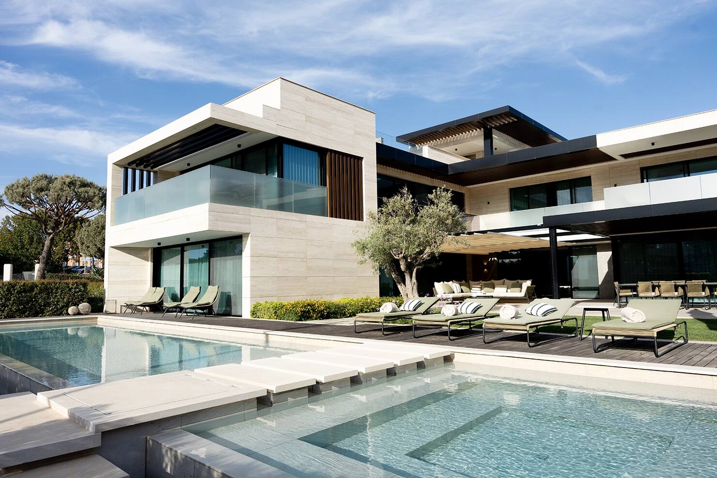 Contemporary stone-clad residence at One Green Way, Quinta do Lago, with a swimming pool, terrace and sun loungers in daylight.