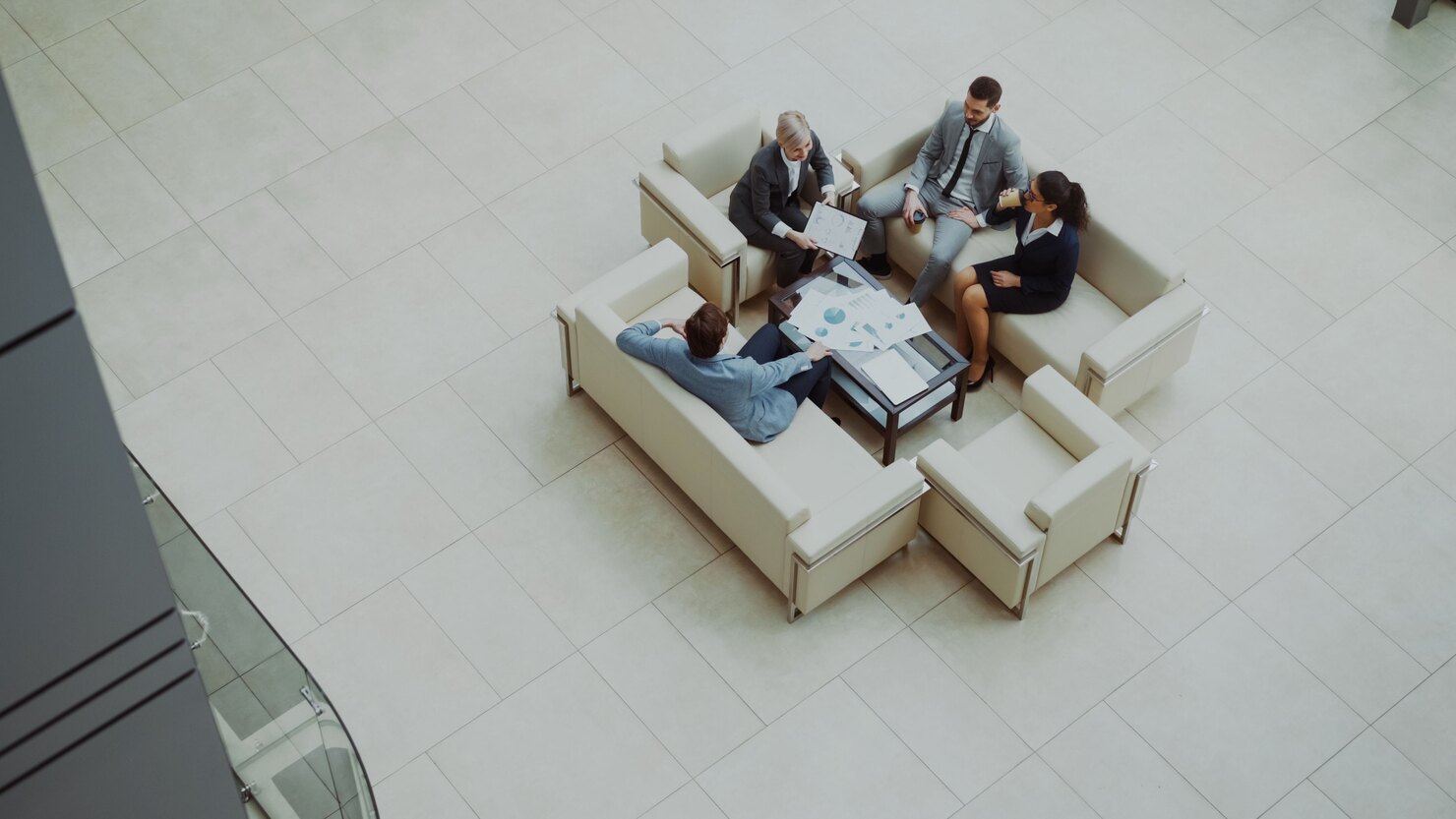 Four advisers reviewing charts and documents during a meeting in a bright office atrium.