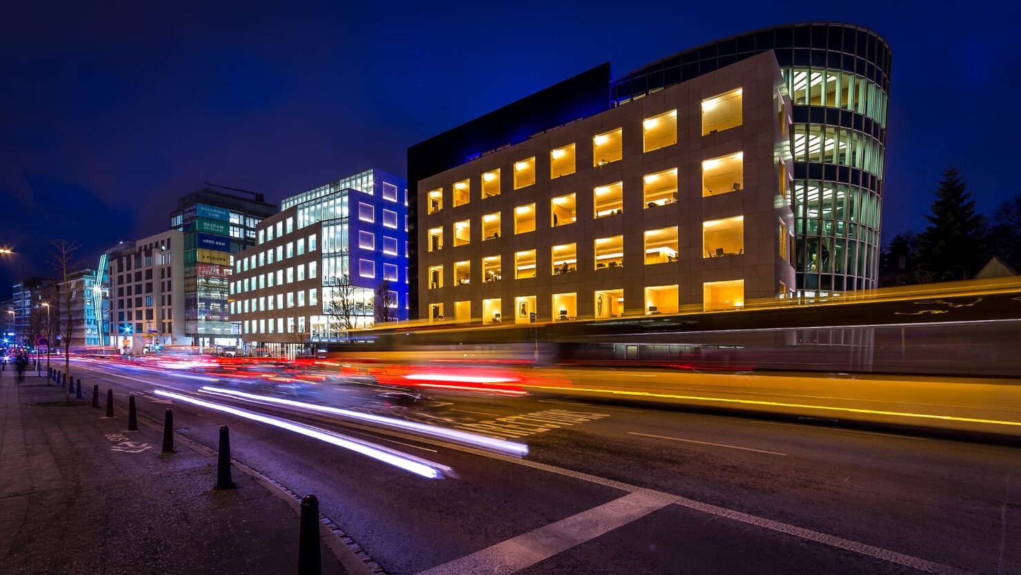 Office buildings lit at night in Luxembourg's business district, with light trails from passing traffic.