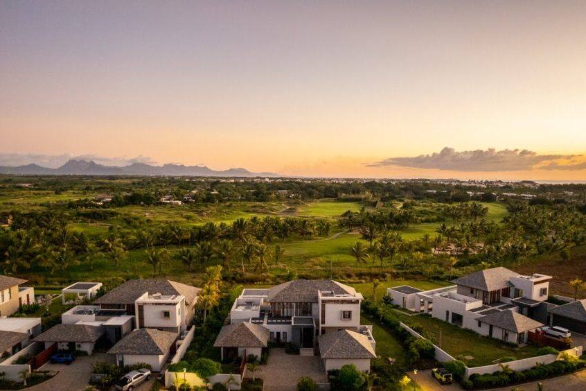 Aerial view at sunset of villas at Mont Choisy Golf & Beach Estate in northern Mauritius, with the golf course and mountains beyond.