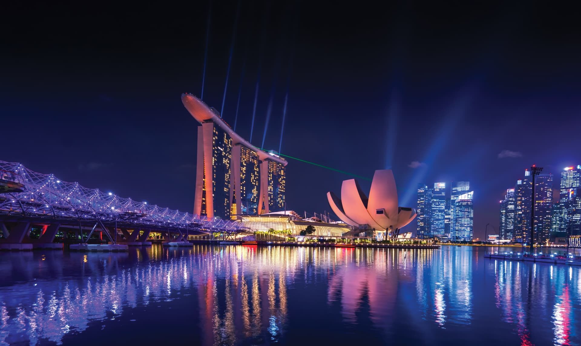 Marina Bay Sands and the Helix Bridge lit at night, reflected in the water of Marina Bay, Singapore.