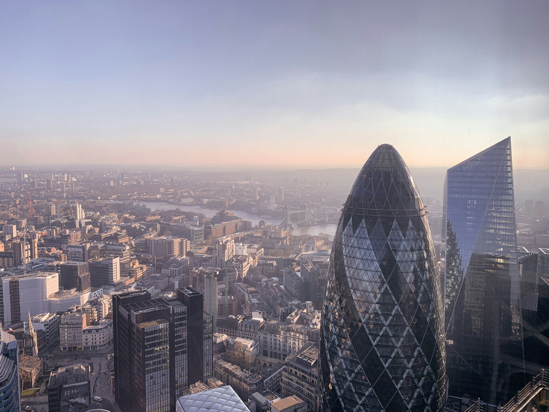 Aerial view across the City of London financial district, with 30 St Mary Axe and the River Thames visible beyond.