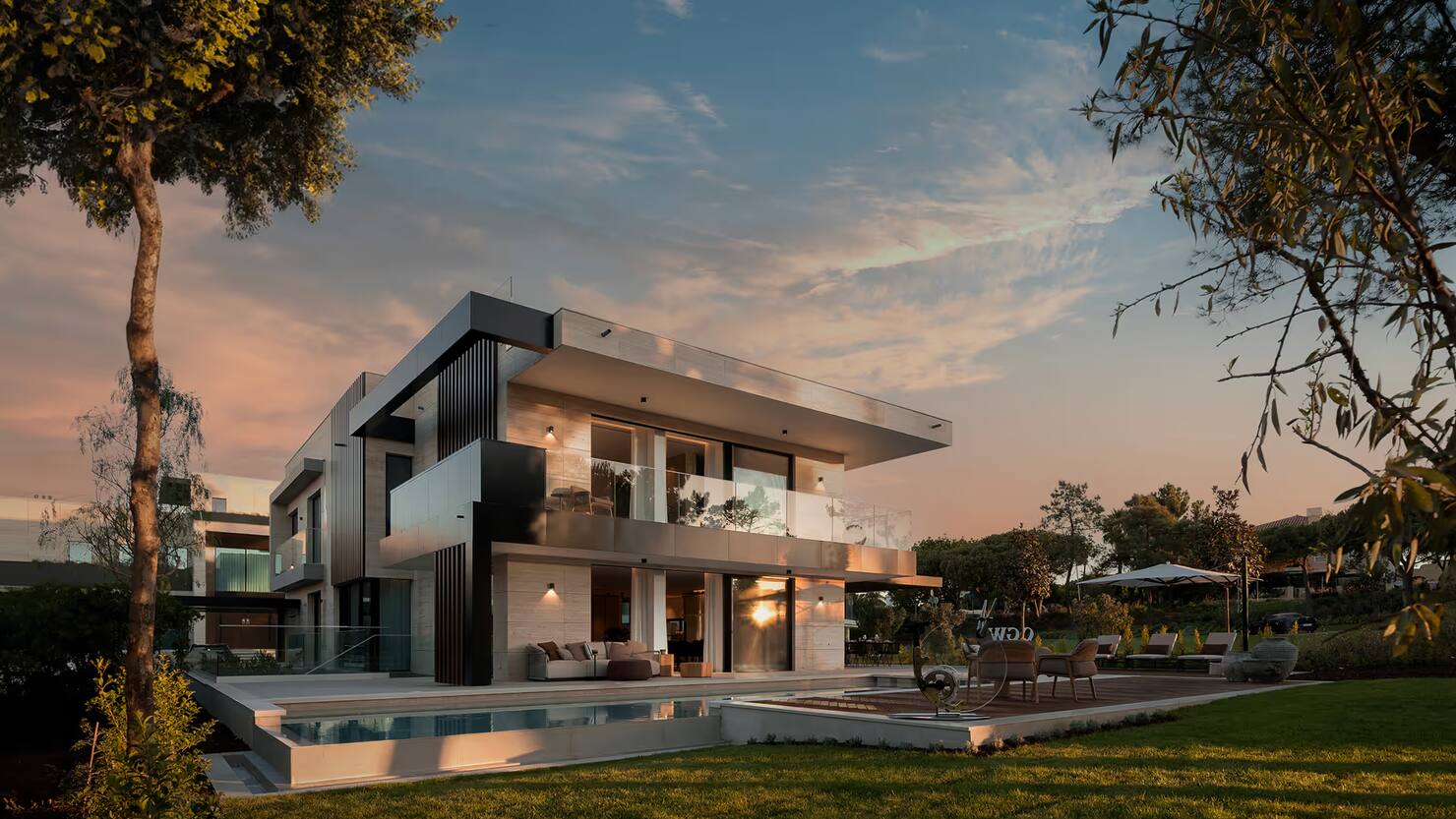 Lit two-storey residence at One Green Way, Quinta do Lago, at dusk, with a pool and lawn in the foreground.