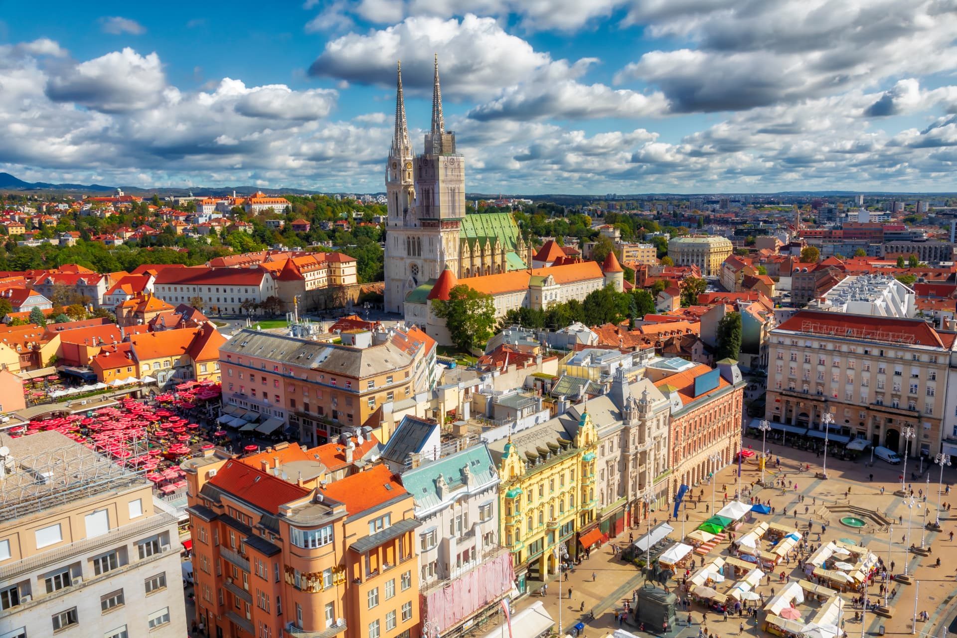 Daytime aerial panorama of Zagreb, Croatia, showing the cathedral spires, red-roofed buildings and hills beyond the city.
